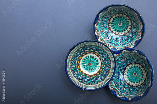 Ethnic Uzbek ceramic tableware on the gray background. Decorative ceramic cups with traditional uzbekistan ornament.