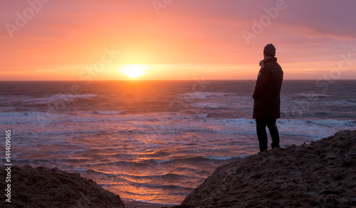 Silhouette of a woman observing sunset the on a deserted beach in Texel, The Netherlands. photo