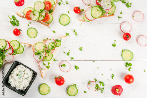 Vegan and healthy diet food: spring vitamin sandwiches with homemade curd cream with herbs, with radishes, cucumbers and tomatoes. On a white wooden table, top view copy space