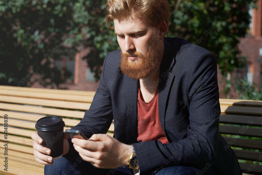 Sad beard man use phone to find new job. Modern hipster drink coffee and surf internet outdoor after study. Concentrated look while playing internet game online on sunny day outdoor. Sad beard man use phone to find new job. Modern hipster drink coffee and surf internet outdoor after study. Concentrated look while playing internet game online on sunny day outdoor.