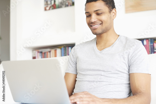Browsing on the internet. full length shot of a smiling young afro American man using a laptop while relaxing in his living room at home.