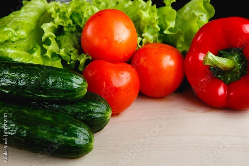 Fresh vegetables on the table: red pepper, lettuce, cucumber, tomatoes. Cutting board