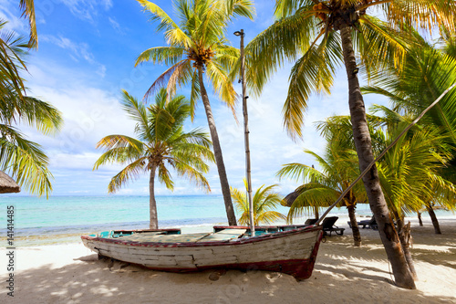 Old wooden fishing boat on a tropical paradise island with coconut palm trees in the background