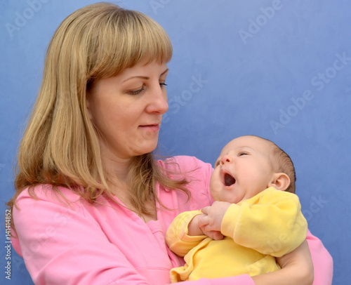 The yawning baby on hands at the young woman on a blue background