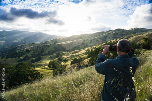Man standing on grassy hill takes photo of sunset in tree covered valley