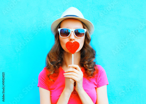 Fashion portrait woman kissing red lollipop shape of a heart over colorful background