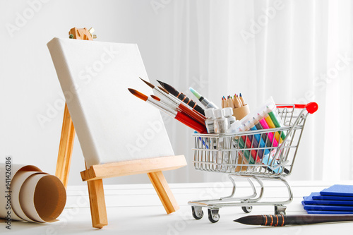 Mini shopping cart full with artistic goods for drawing, artist canvas and easel. Art shop concept.