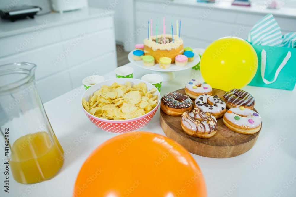 Doughnuts, potato chip, birthday cake and balloons on table Doughnuts, potato chip, birthday cake and balloons on table