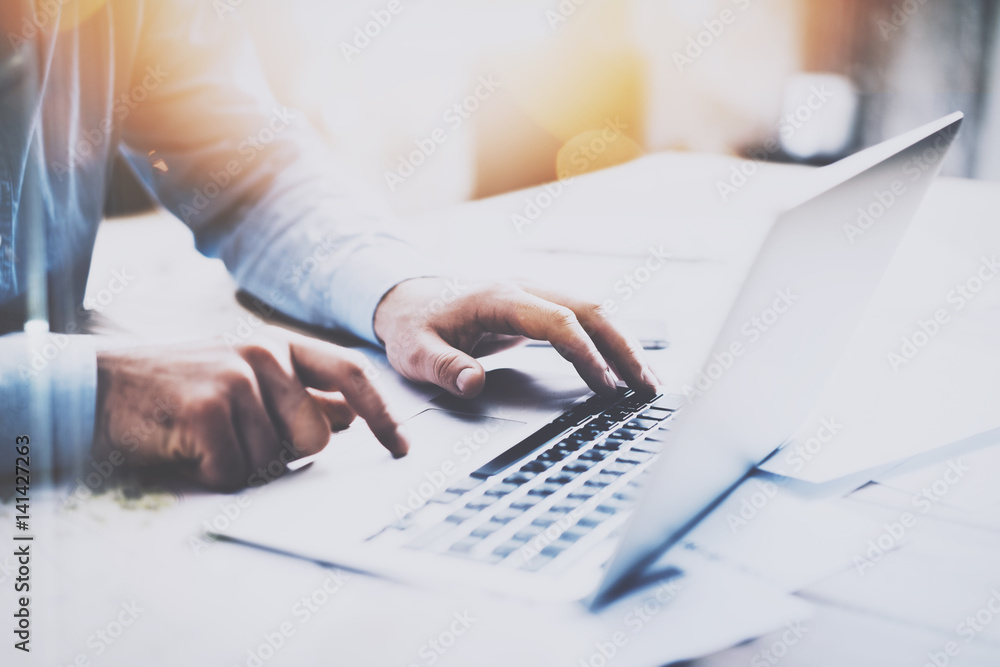 Man working at the wooden table at modern loft office.Man sitting at workplace and typing on laptop keyboard.Blurred background.Horizontal,visual effects. Man working at the wooden table at modern loft office.Man sitting at workplace and typing on laptop keyboard.Blurred background.Horizontal,visual effects.
