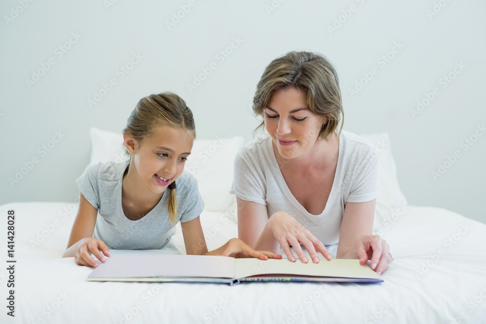 Mother and daughter lying on bed and reading book Mother and daughter lying on bed and reading book