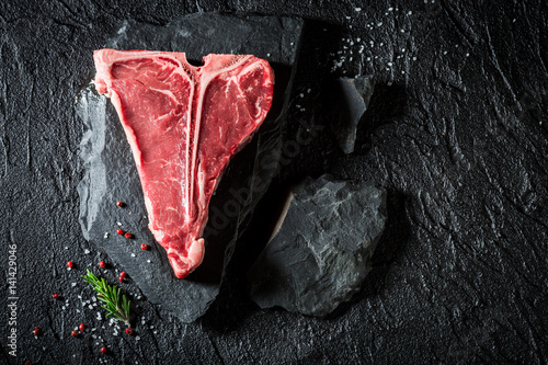Fényképezés Fresh t-bone steak on black rock with salt and pepper