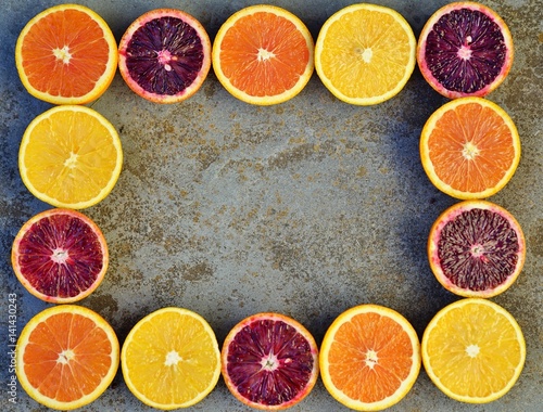 Oranges, blood oranges, and cara cara oranges cut in half forming a border frame on a stone background