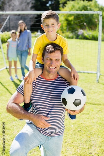 father with football carrying his son on shoulder