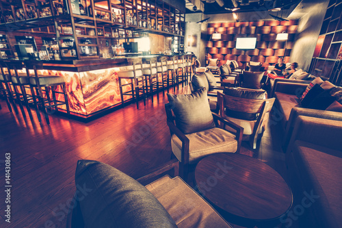 A modern restaurant cafe interior with chair, table, sofa, lighting and bar decoration wall with alcohol ssortment. Concept of relaxing outside and communication. Vintage toning, dark lights photo