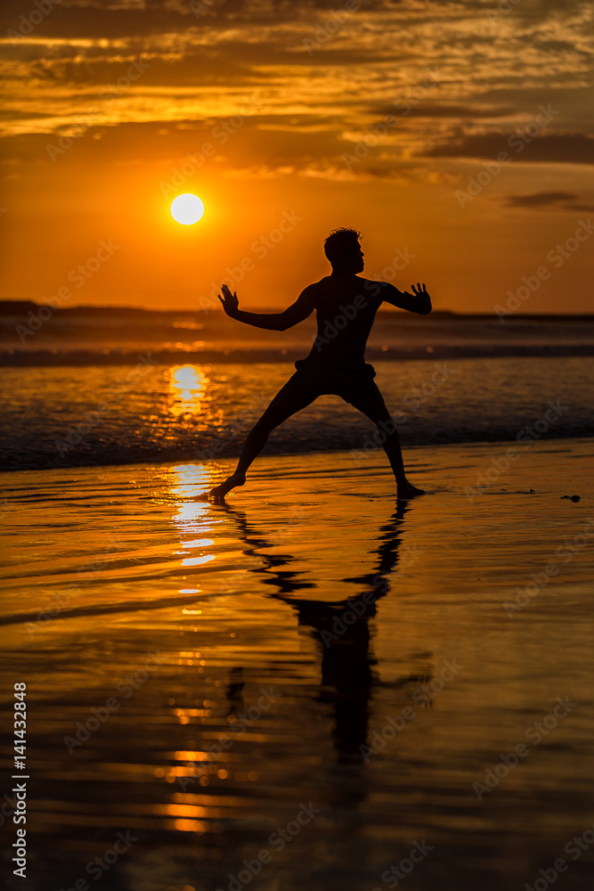 Silhouette of young male capoeira dancer, yoga and martial art specialist at beach in Mexico during spectacular sunset