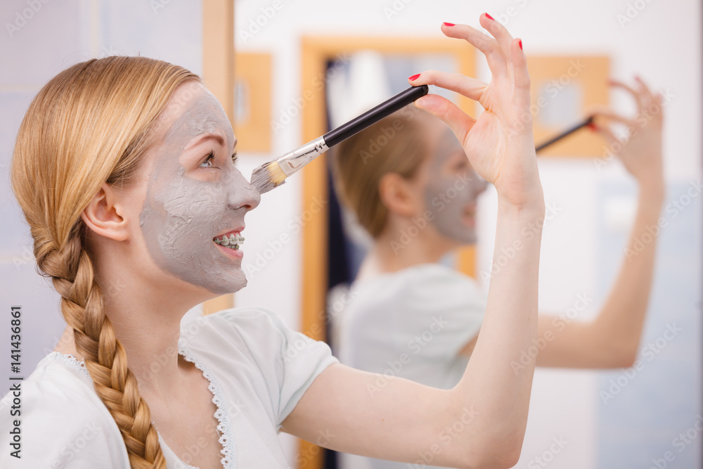 Happy young woman applying mud mask on nose