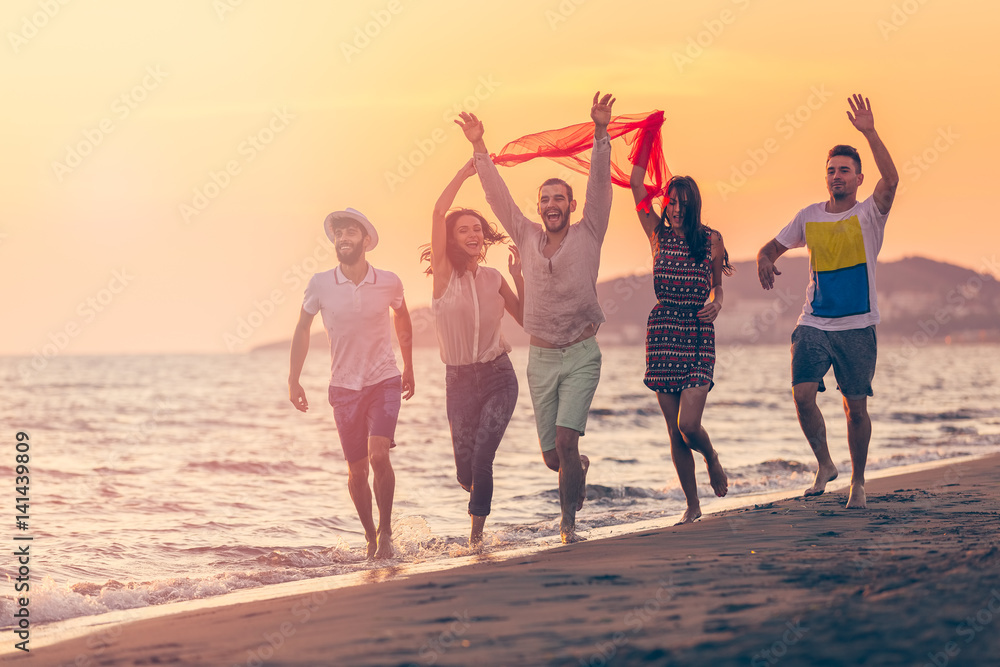 Group of happy young people is running on background of sunset beach and sea Group of happy young people is running on background of sunset beach and sea