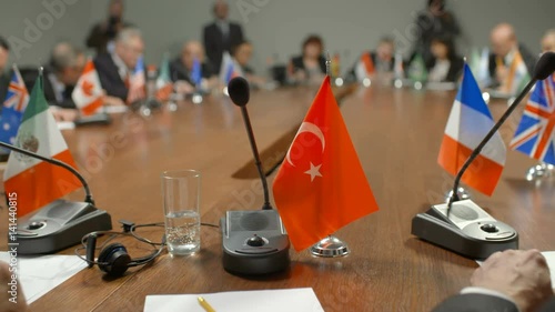 Turkish delegation at international summit or conference. Representatives of the Turkish government surrounded by other politicians give a speech at the round table. Audience applaud the speaker and