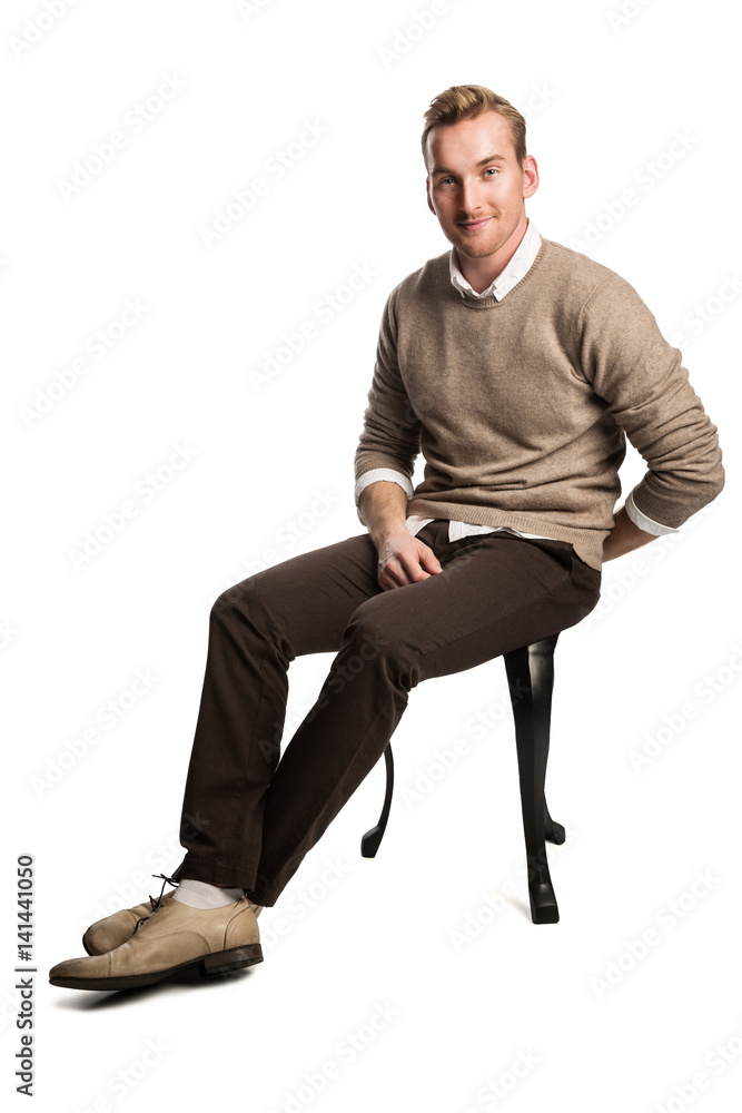 Handsome blonde man wearing a brown pullover and white shirt, sitting down smiling against a white background. Handsome blonde man wearing a brown pullover and white shirt, sitting down smiling against a white background.