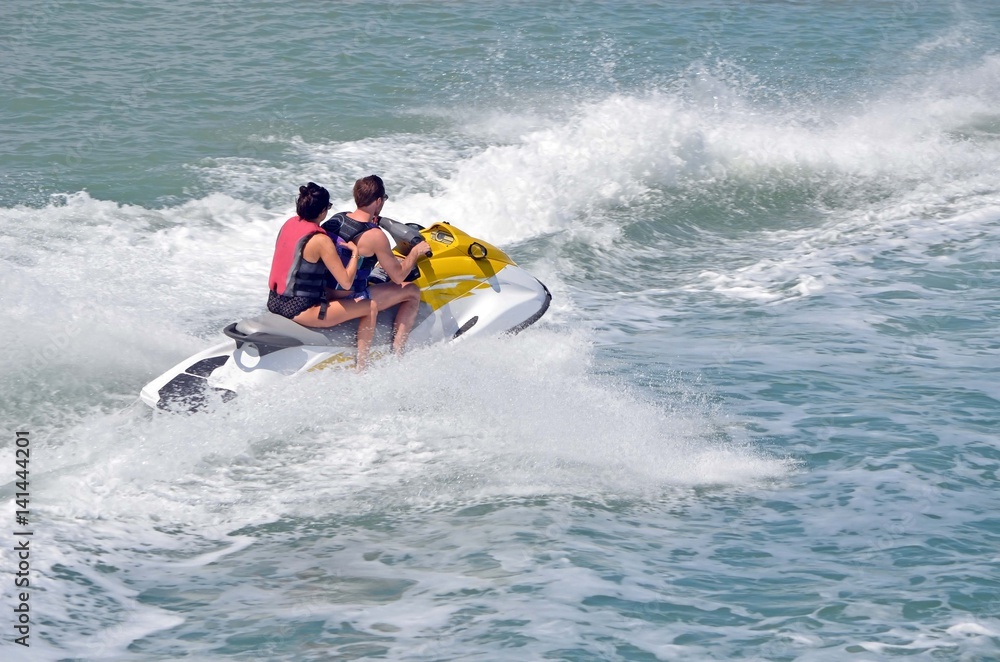 Young man and woman riding tandem on a  speeding jet ski.