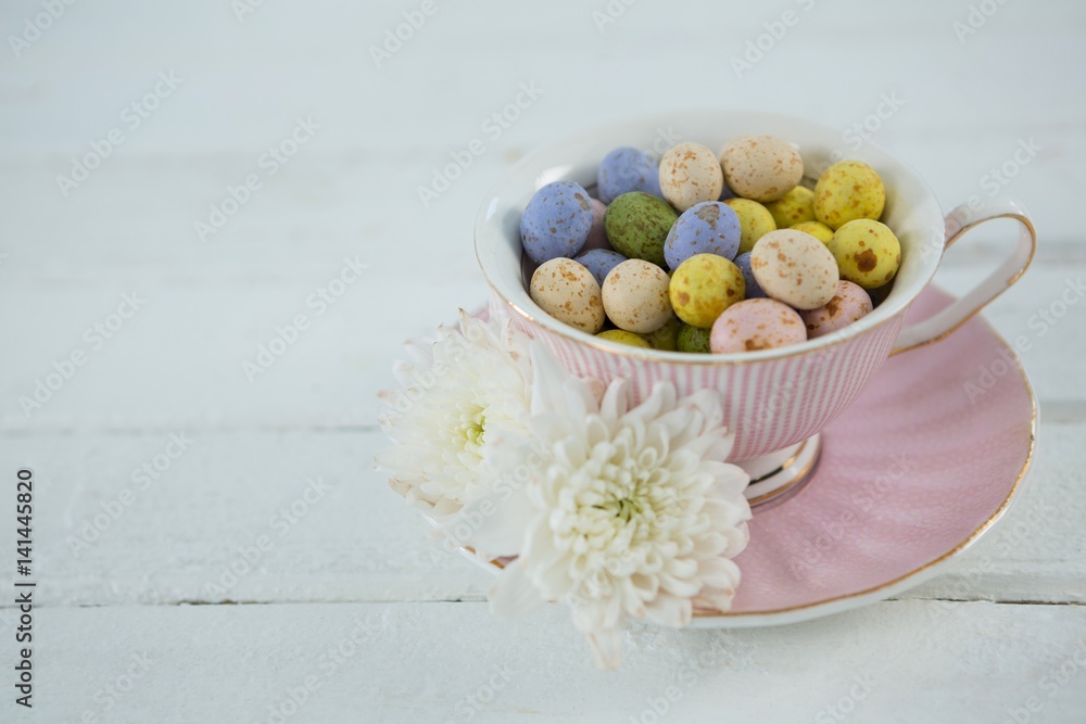 Cup filled with colorful chocolate Easter eggs and white flower Cup filled with colorful chocolate Easter eggs and white flower