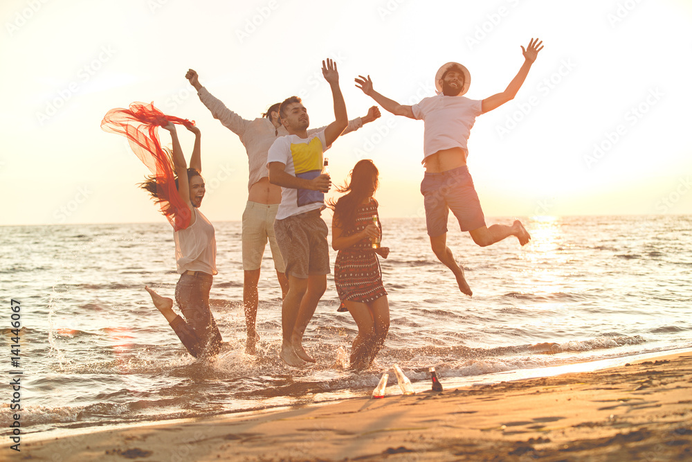 group of happy young people dancing at the beach on beautiful summer sunset - obrazy, fototapety, plakaty 