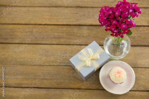 Gift box and flower vase with cupcake in plate on wooden plank