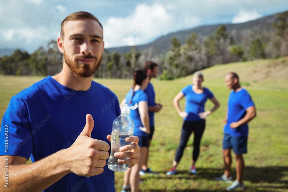 Fototapeta premium Fit man showing thumbs up while holding water bottle