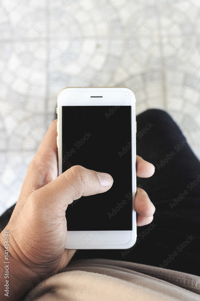 mockup image of hands holding white mobile phone with blank black screen, soft-focus in the background. over light and film colors tone