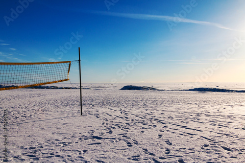 Volleyball net on the deserted snow covered beach on sunny winter day.