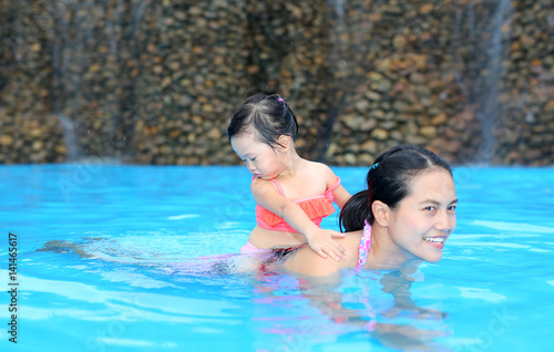 Pretty little girl with her mother in swimming pool outdoors