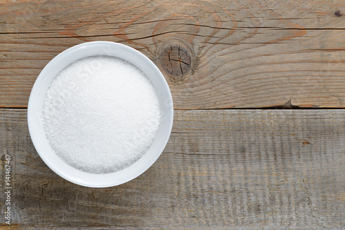 White sugar in bowl on wooden table top view