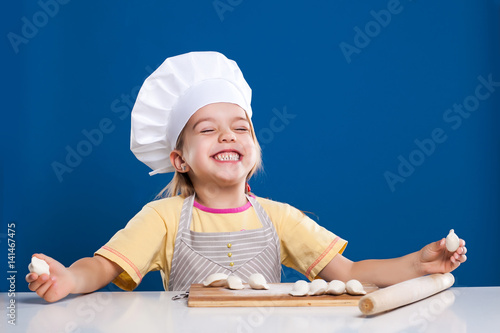 The little girl is cooking and preparing food on blue background