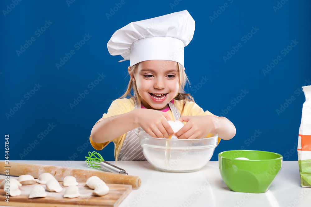 The little girl is cooking and preparing food on blue background The little girl is cooking and preparing food on blue background