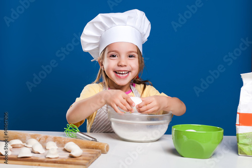The little girl is cooking and preparing food on blue background