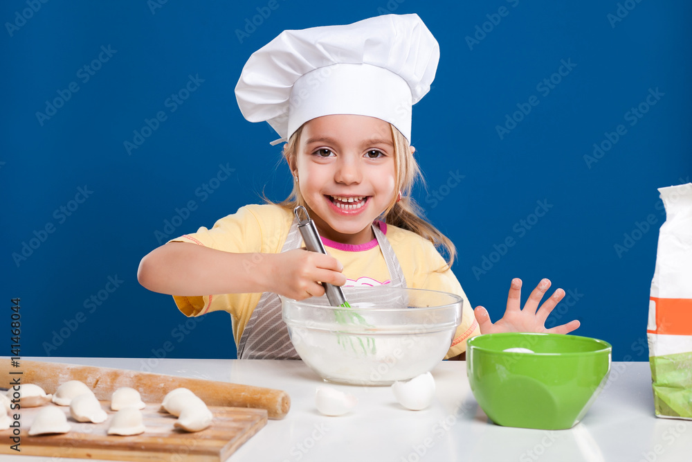 The little girl is cooking and preparing food on blue background The little girl is cooking and preparing food on blue background