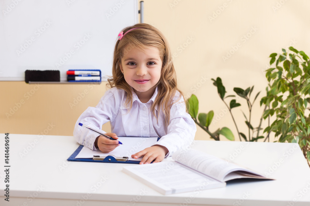 Beautiful little girl writes sitting at table Beautiful little girl writes sitting at table