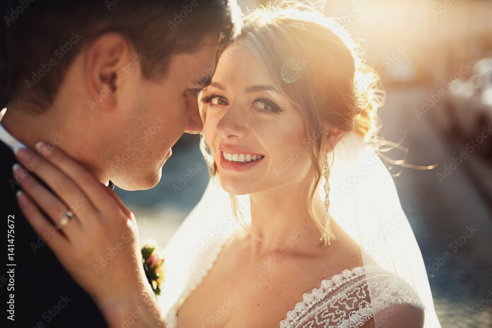 Groom leans to bride's happy face hugging her on an old street Groom leans to bride's happy face hugging her on an old street