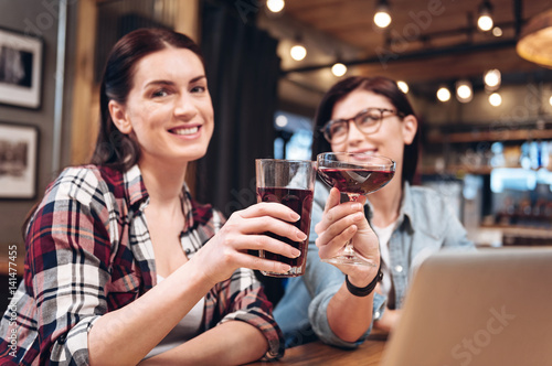Portrait of positive woman while clinking glasses with her friend
