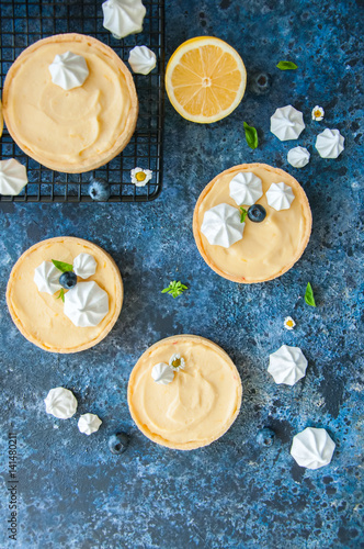 Lemon curd and blueberry jam tarts with meringue and basil leaves Chamomiles whole and slices of fresh lemon on a blue rusty textured background. Copy Space. Flat lay. Top View.