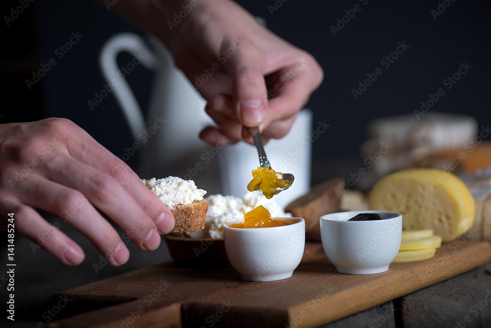 Man's hand putting jam from bowl on bread with ricotta cheese Man's hand putting jam from bowl on bread with ricotta cheese
