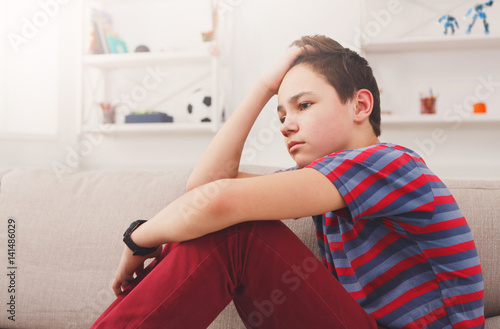 Fotografie Bored unhappy teenage boy sitting at home