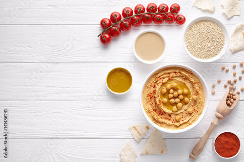 Hummus homemade arabic healthy vegan dip chickpeas paste snack flat lay with ingridients, tahini, paprika, olive oil, cherrys, pitta bread on white table. Healthy vegetarian nutrition food