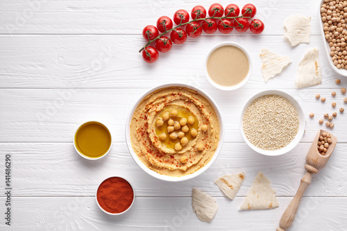 Hummus traditional Mediterranean healthy vegan dip chickpeas paste snack flat lay with natural ingridients, tahini, paprika, olive oil, pitta on table. Healthy vegetarian diet nutrition protein food