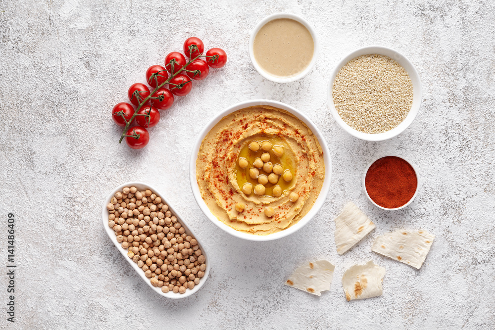 Hummus flat lay with ingridients, healthy diet natural vegetarian snack protein food. Traditional eastern arab appetizer. Sesame, paprika, tahini, pita bread and olive oil on white table background Hummus flat lay with ingridients, healthy diet natural vegetarian snack protein food. Traditional eastern arab appetizer. Sesame, paprika, tahini, pita bread and olive oil on white table background
