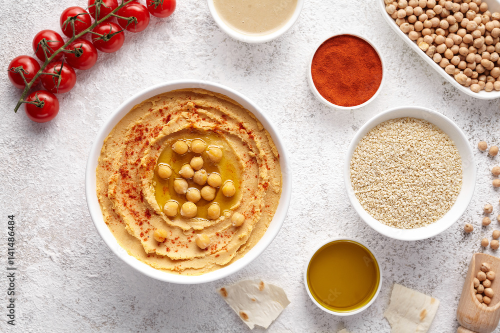 Chickpea hummus flat lay with ingridients, healthy diet natural vegetarian snack protein food. Traditional mediterranean appetizer. Sesame, paprika, tahini, pita bread and olive oil on white table Chickpea hummus flat lay with ingridients, healthy diet natural vegetarian snack protein food. Traditional mediterranean appetizer. Sesame, paprika, tahini, pita bread and olive oil on white table