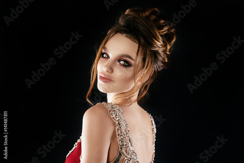 Beautiful  sexy brunette girl with big lips  hair and makeup in a long burgundy dress with precious stones. In a staged on a gray background  a place for advertising