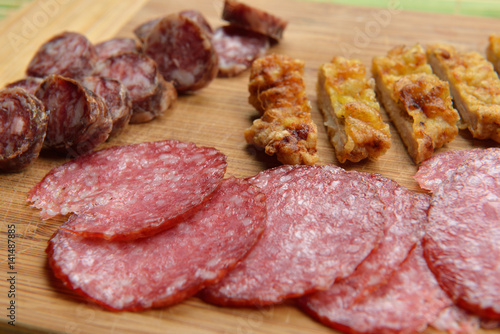 Different meat products (sausages, salami, breaded chicken breast) arranged on a wood trencher. Rustic food. Selective focus