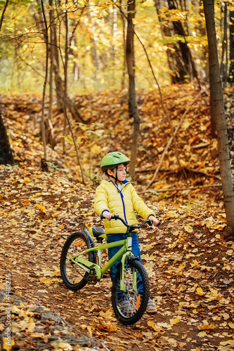 A boy is riding a bicycle in an autumn forest.