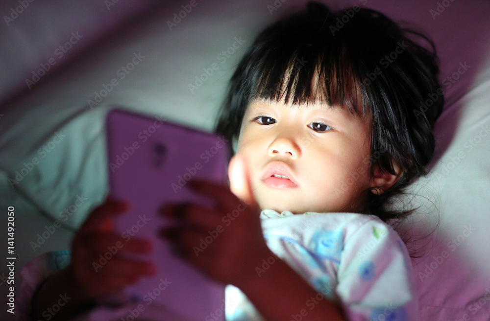 Cute little girl in pajamas playing smartphone lying on a bed Cute little girl in pajamas playing smartphone lying on a bed